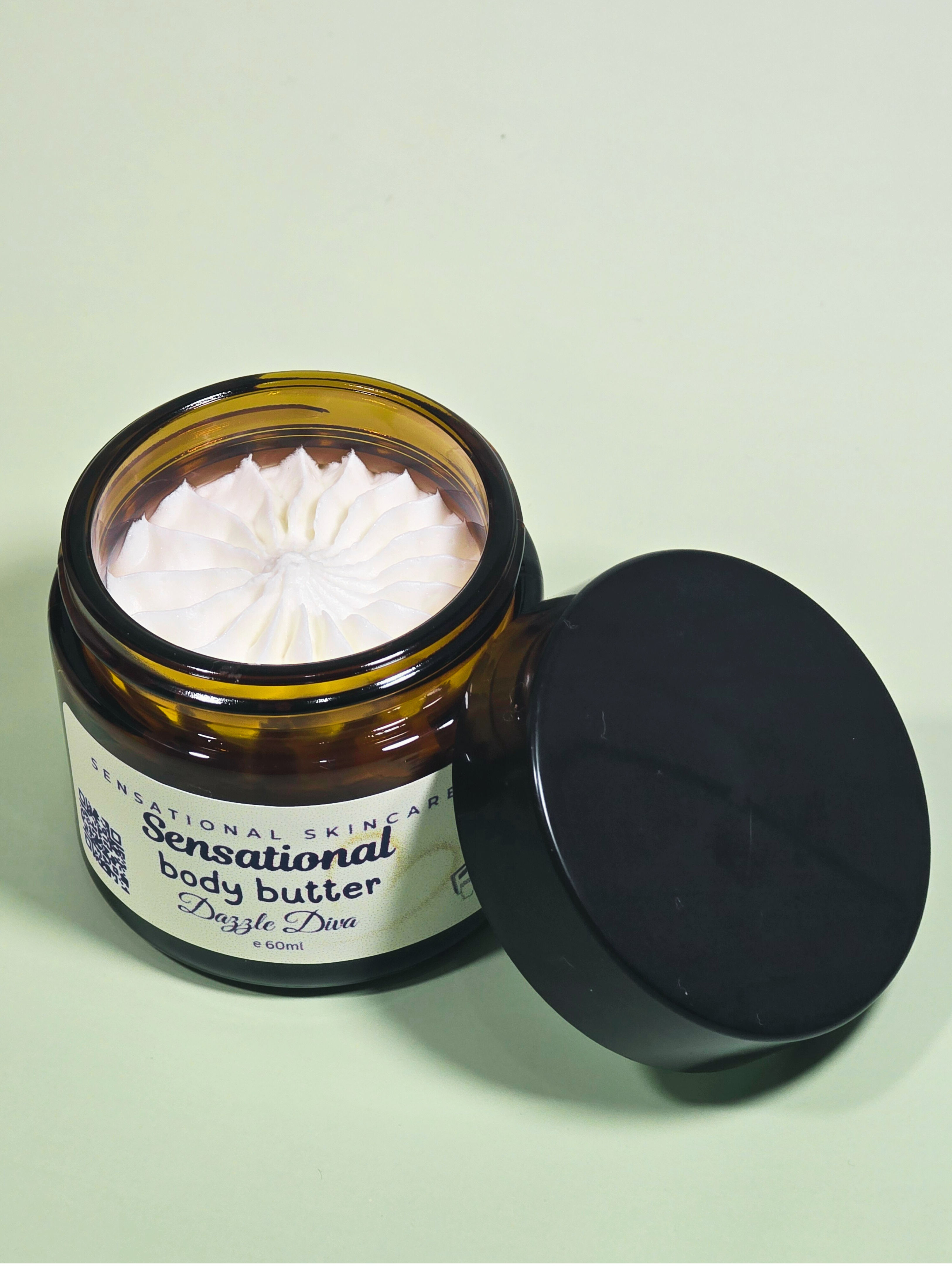 Open jar of Sensational Skincare body butter with a black lid on a light green background