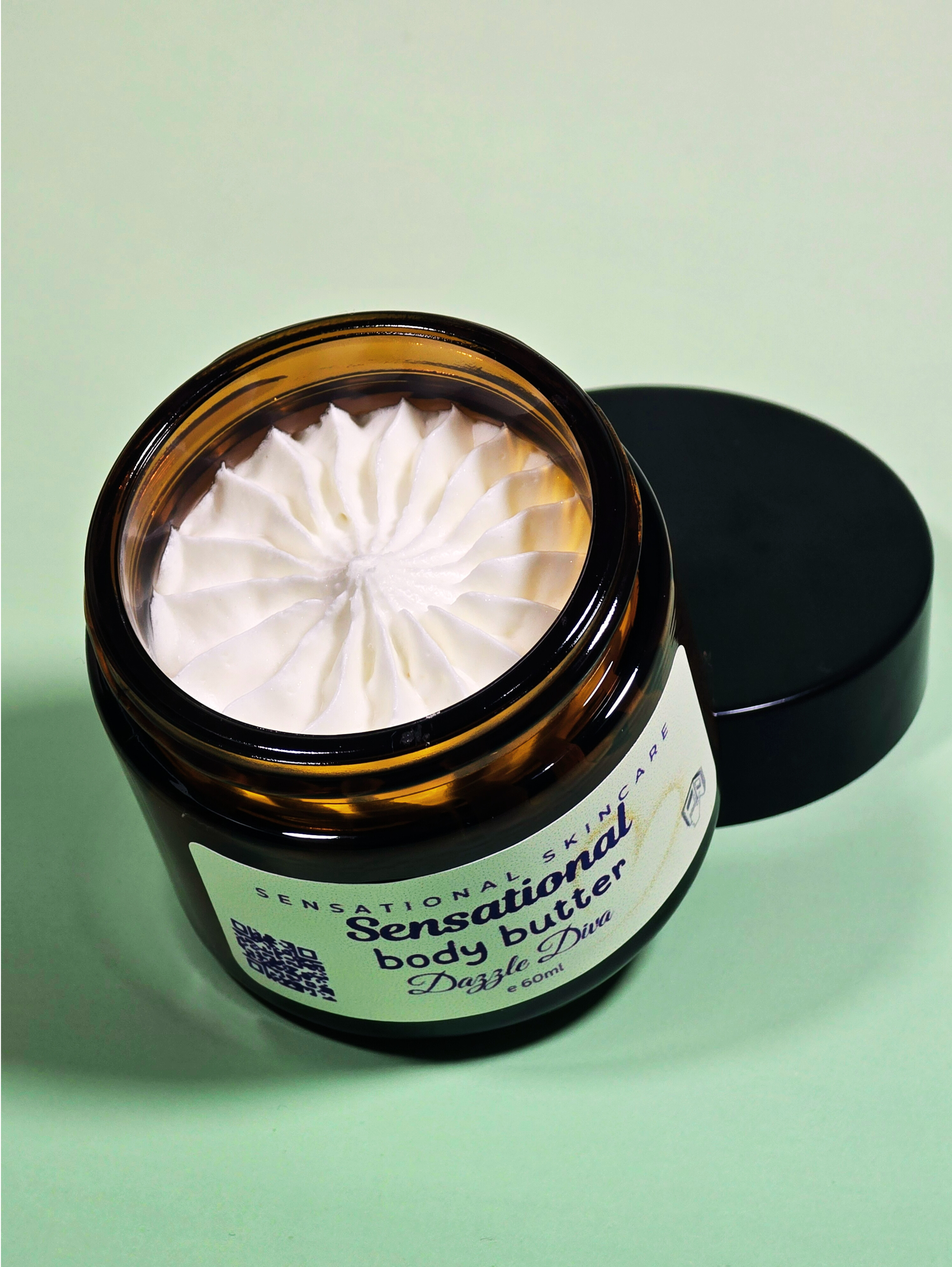 Open jar of Sensational Body Butter with a green background